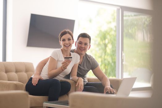 happy young couple buying online using laptop a computer and a credit card in their luxury home villa