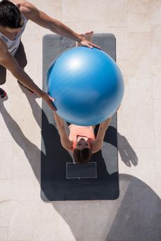 young beautiful woman and personal trainer doing exercise with pilates ball in front of her luxury home