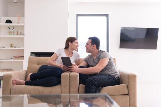 Young couple relaxing at luxurious home with tablet computers reading in the living room on the sofa couch.