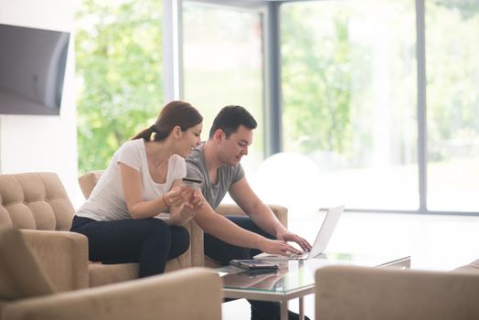 happy young couple buying online using laptop a computer and a credit card in their luxury home villa