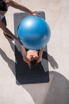 young beautiful woman and personal trainer doing exercise with pilates ball in front of her luxury home