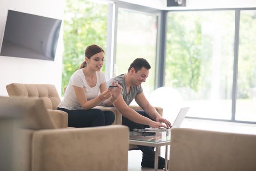 happy young couple buying online using laptop a computer and a credit card in their luxury home villa