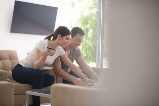 happy young couple buying online using laptop a computer and a credit card in their luxury home villa