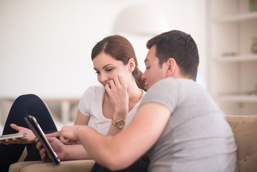 Young couple relaxing at luxurious home with tablet computers reading in the living room on the sofa couch.