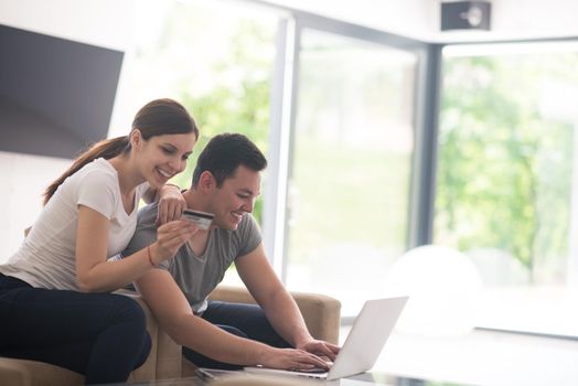 happy young couple buying online using laptop a computer and a credit card in their luxury home villa