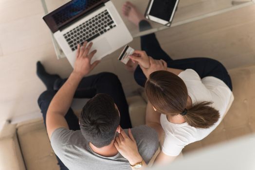 happy young couple buying online using laptop a computer and a credit card in their luxury home villa