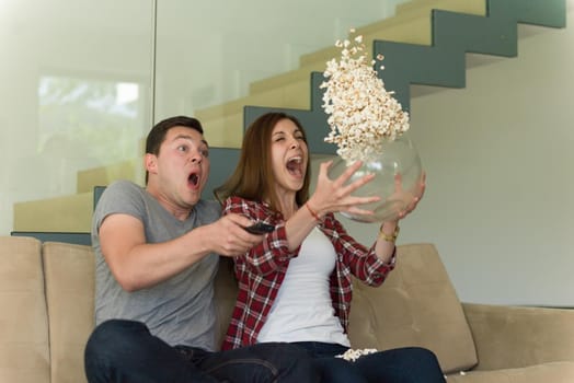 young handsome couple enjoying free time watching television with popcorn in their luxury home villa