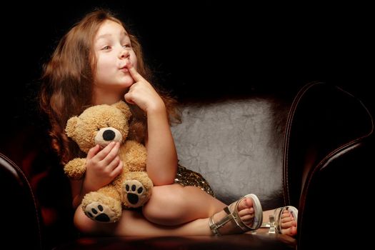 A nice little girl with a teddy bear. Studio photo on a black background. The concept of a happy childhood, publication on the cover of the magazine.