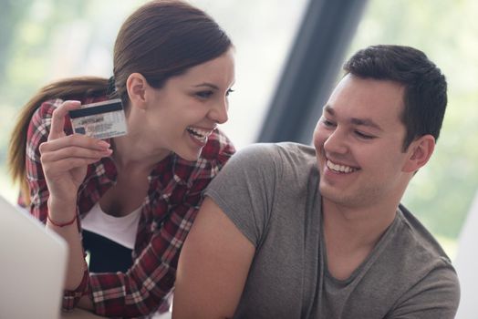 happy young couple buying online using laptop a computer and a credit card in their luxury home villa