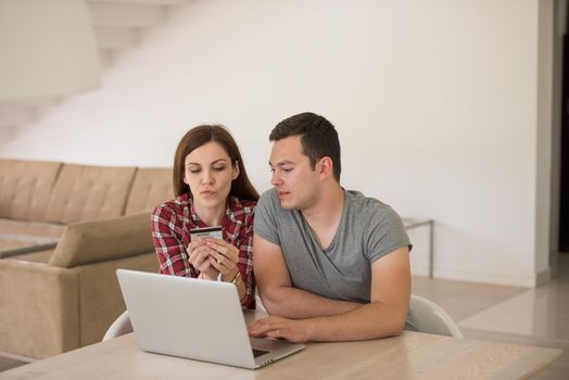 happy young couple buying online using laptop a computer and a credit card in their luxury home villa