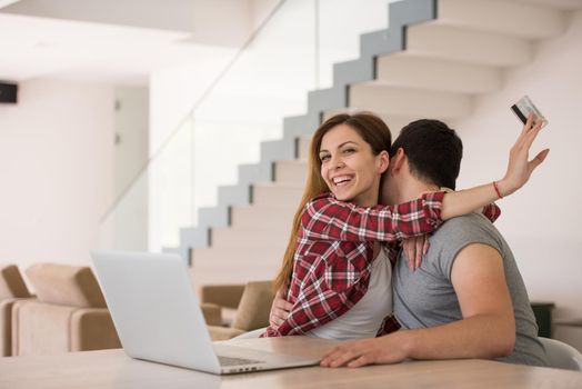 happy young couple buying online using laptop a computer and a credit card in their luxury home villa