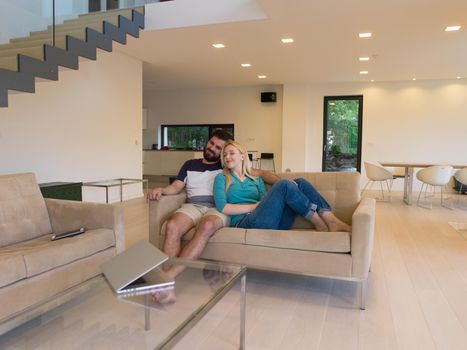 Young couple relaxes on the sofa in the luxury living room, using a laptop and remote control