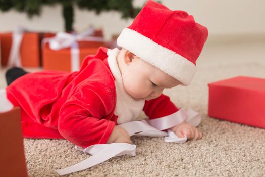 Beautiful little baby celebrates Christmas. New Year's holidays. Baby in a Christmas costume and in santa hat and gift box.