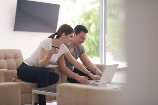 happy young couple buying online using laptop a computer and a credit card in their luxury home villa