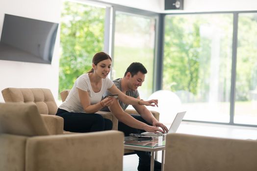 happy young couple buying online using laptop a computer and a credit card in their luxury home villa