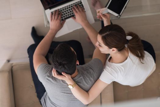 happy young couple buying online using laptop a computer and a credit card in their luxury home villa