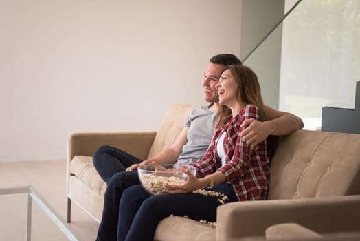 young handsome couple enjoying free time watching television with popcorn in their luxury home villa