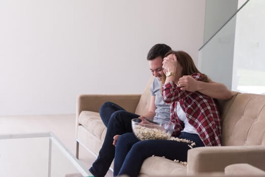 young handsome couple enjoying free time watching television with popcorn in their luxury home villa