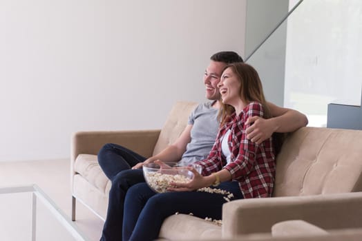 young handsome couple enjoying free time watching television with popcorn in their luxury home villa