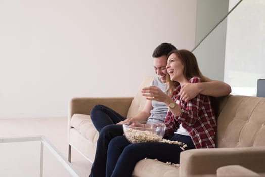 young handsome couple enjoying free time watching television with popcorn in their luxury home villa