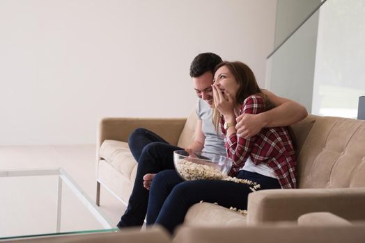 young handsome couple enjoying free time watching television with popcorn in their luxury home villa