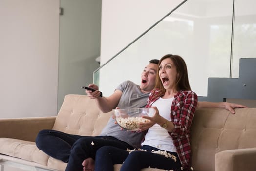 young handsome couple enjoying free time watching television with popcorn in their luxury home villa