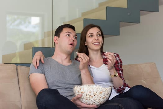 young handsome couple enjoying free time watching television with popcorn in their luxury home villa