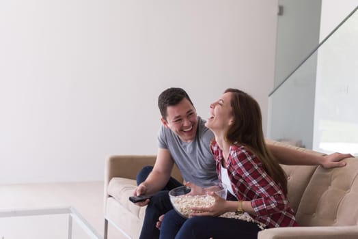 young handsome couple enjoying free time watching television with popcorn in their luxury home villa