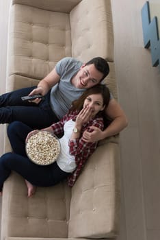 young handsome couple enjoying free time watching television with popcorn in their luxury home villa