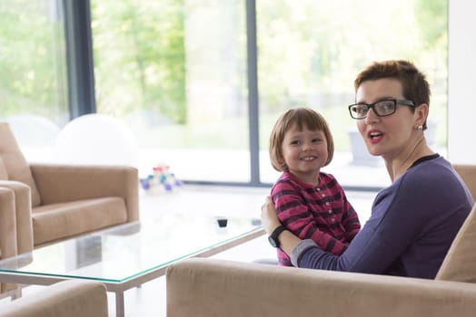 young mother and cute little girl enjoying their free time hugging on the sofa in their luxury home villa