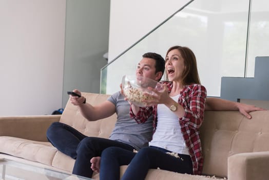 young handsome couple enjoying free time watching television with popcorn in their luxury home villa