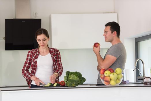 Young handsome couple in the kitchen  beautiful woman preparing a salad while the man eating an apple