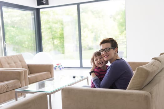 young mother and cute little girl enjoying their free time hugging on the sofa in their luxury home villa