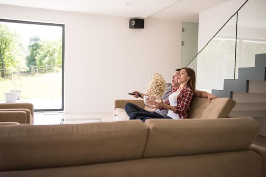 young handsome couple enjoying free time watching television with popcorn in their luxury home villa