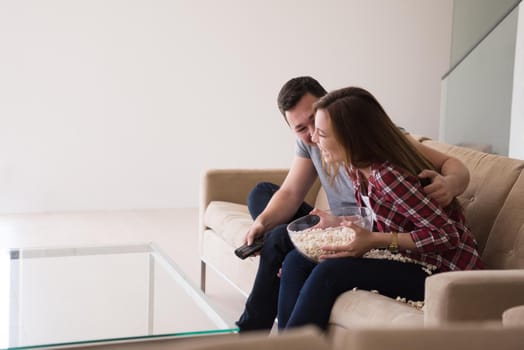 young handsome couple enjoying free time watching television with popcorn in their luxury home villa