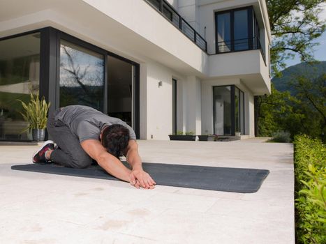 young handsome man doing morning yoga exercises in front of his luxury home villa