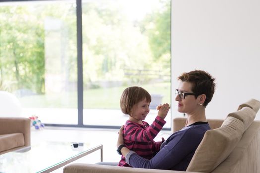 young mother and cute little girl enjoying their free time hugging on the sofa in their luxury home villa