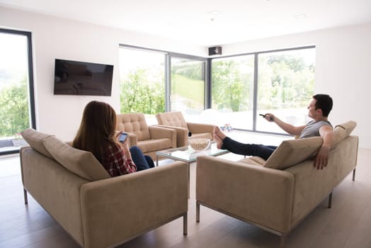 young handsome couple enjoying free time watching television with popcorn in their luxury home villa