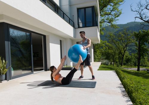 young beautiful woman and personal trainer doing exercise with pilates ball in front of her luxury home