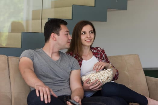 young handsome couple enjoying free time watching television with popcorn in their luxury home villa