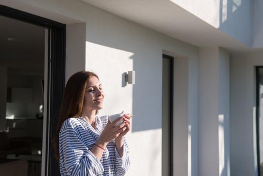 young beautiful woman in a bathrobe enjoying morning coffee in front of her luxury home villa