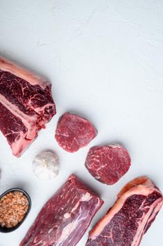 Fresh raw Prime Black Angus beef marbled and dry aged steaks set, tomahawk, t bone, club steak, rib eye and tenderloin cuts, on white stone background, top view flat lay, with copy space for text