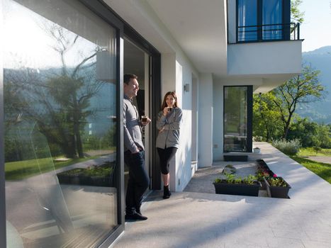 young beautiful handsome couple enjoying morning coffee on the door of their luxury home villa