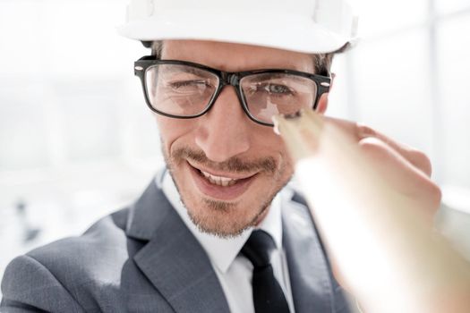 Builder. Mechanic in construction helmet holds construction ruler near face. Man with construction roulette.