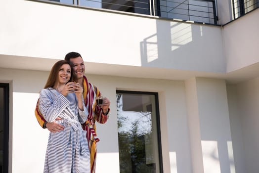 Young beautiful couple in bathrobes are enjoying morning coffee in front of their luxury home villa