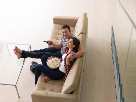 young handsome couple enjoying free time watching television with popcorn in their luxury home villa