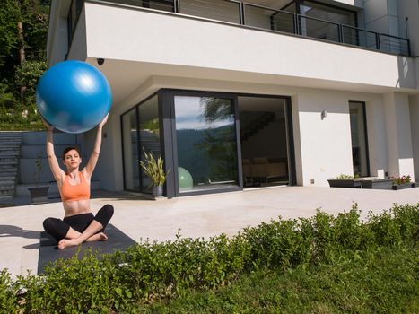 young beautiful woman doing exercise with pilates ball in front of her luxury home villa