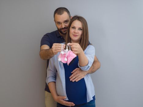 young  pregnant couple holding newborn baby shoes isolated on white background in family and parenthood concept