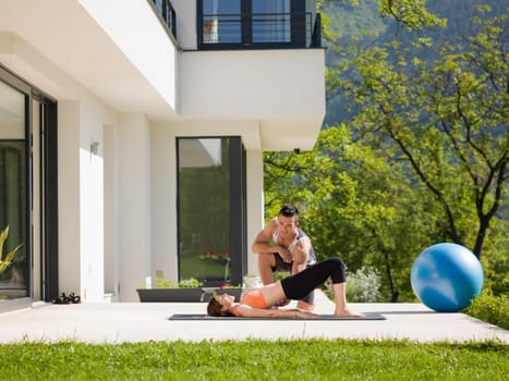 young handsome woman with personal trainer doing morning yoga exercises in front of her luxury home villa