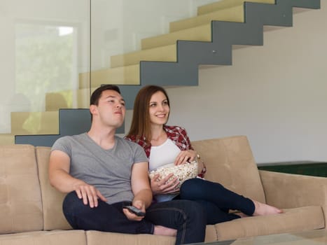 young handsome couple enjoying free time watching television with popcorn in their luxury home villa